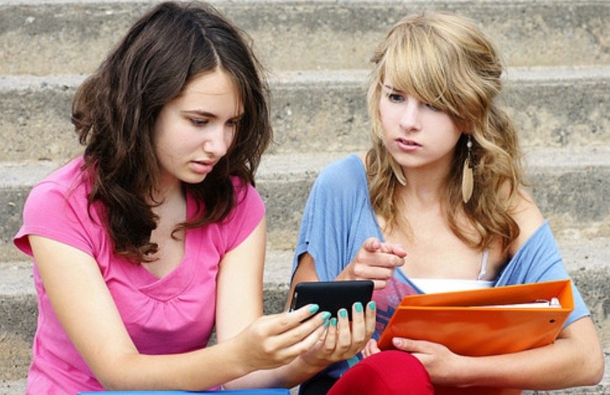Two students on concrete steps, looking at a phone together.